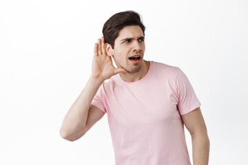 Gossip man trying to overhear someone, hold hand near ear and lean closer to copy space, trying to understand words, eavesdropping, standing over white background
