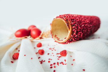 Traditional Hungarian kurtos kalacs with raspberry flavor known as chimney cake on a rustic tablecloth and red Easter eggs. 
