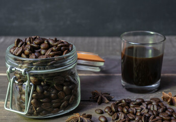 Coffee beans in jar with black coffee in glass on rustic wooden table.Coffee vintage promo concept on dark background with copy space for text.