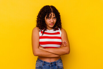 Young mixed race woman isolated on yellow background blows cheeks, has tired expression. Facial expression concept.