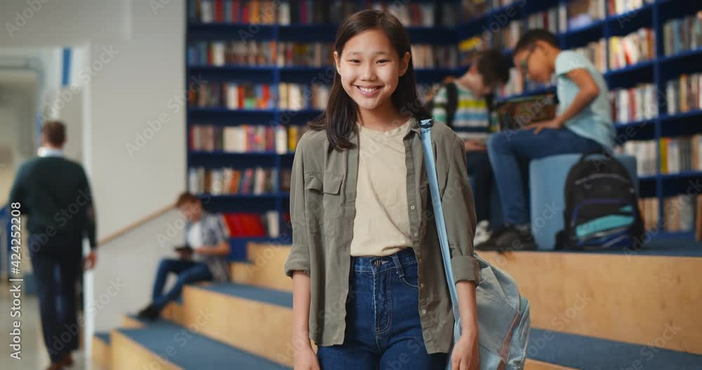 Canvas Prints Portrait of smiling asian schoolgirl looking at camera standing in library