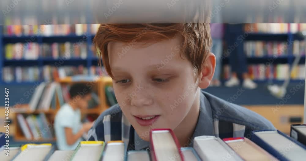 Poster close up of redhead cute schoolboy taking book from bookshelf in library