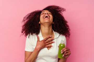 Young african american woman drinking a healthy smoothie isolated on pink background laughs out...