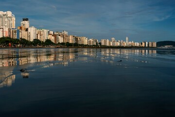 Fototapeta premium Late afternoon at Santos beach with waterfront buildings illuminated by sunlight in the blue sky.