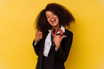 Young African American air hostess isolated on yellow background raising both thumbs up, smiling...