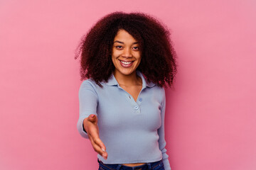 Young african american woman isolated on pink background stretching hand at camera in greeting gesture.