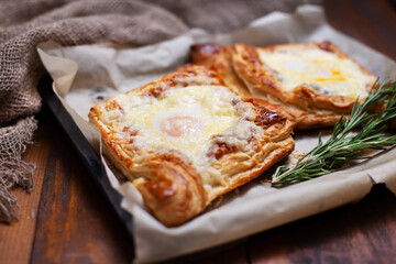Homemade georgian cheese pastry and eggs with rosemary on baking paper on burlap cloth and brown wooden table.