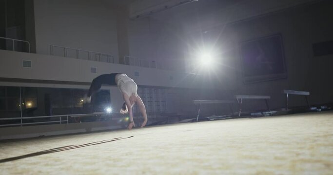 Girl gymnast performs somersaults forward in the gym on a gymnastic mat night training preparation for competitions