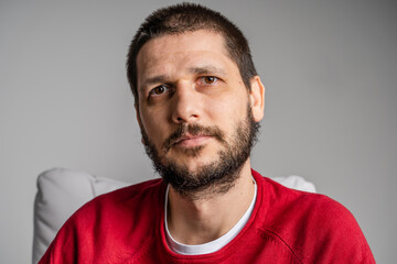 Fototapeta premium Front view close up portrait of adult caucasian man with beard and dark brown hair looking to the camera - serious confused male face sitting