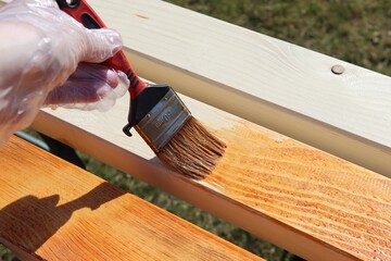 Photo of a hand painting a wooden beam with brown glazing varnish. Brush in the hands of the...