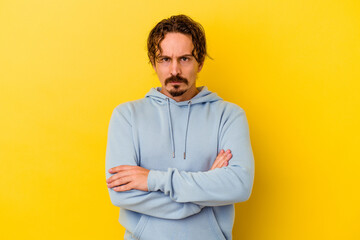 Young caucasian man isolated on yellow background frowning face in displeasure, keeps arms folded.