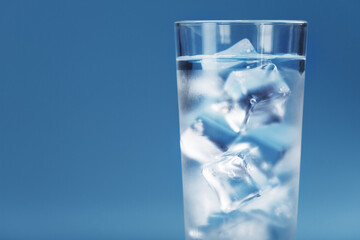 A glass with ice and clean water on a blue background.
