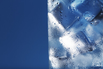 Ice cubes in a glass with crystal clear water on a blue background.