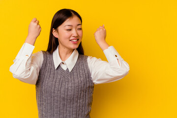 Young chinese woman isolated on yellow background raising fist after a victory, winner concept.