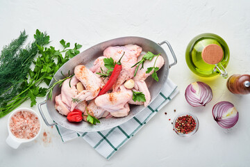 Raw chicken wings in a white bowl with spices and ingredients for cooking on light slate, stone or concrete background. Top view with copy space. Mock up.