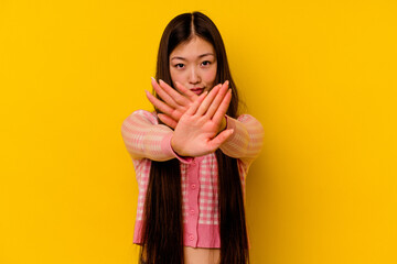 Young chinese woman isolated on yellow background doing a denial gesture