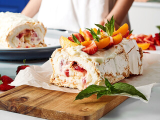 Meringue roll with a delicate air cream, mint and fruit filling of strawberries, peaches and mint. Pavlova summer sweet dessert. Berry dessert on the background of a girl. Summer baking. Copy space.