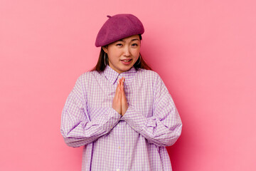 Young chinese woman isolated on pink background holding hands in pray near mouth, feels confident.