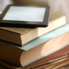 Stack of vintage hardcover books and e-reader on top. Selectve focus.