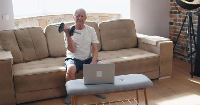 adult man and mature senior working his body with dumbbell - one man hapy training indoors sitted on the sofa. High quality 4k footage