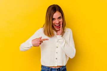 Young caucasian skinny woman isolated on yellow background saying a gossip, pointing to side reporting something.