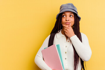 Young african american student woman isolated on yellow background looking sideways with doubtful...