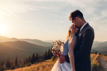 Loving wedding couple hugging in mountains at sunset. Portrait of young bride and groom in summer...