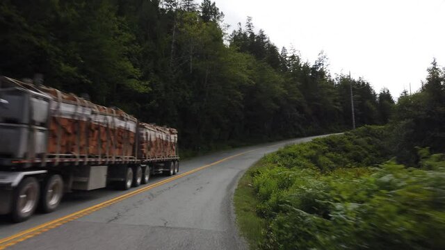 Slow motion gimbal driving shot of a truck full of tree logs during summer