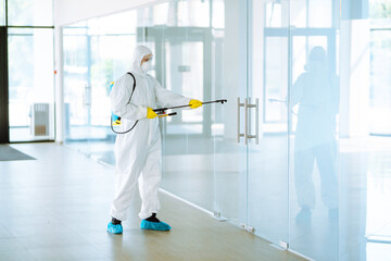 Man in Hazmat suit, protective gloves and goggles use sprayer equipment disinfect  in office....