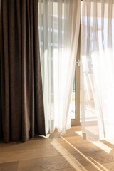 Modern room interior with an open window in minimal style. Transparent tulle with morning sun rays on shadow background. Vertical photo