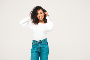 Beautiful black woman with afro curls hairstyle.Smiling model in sweater and trendy jeans clothes. Sexy carefree female posing on white background in studio. Tanned and cheerful