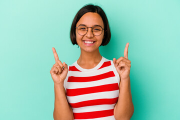 Young mixed race woman isolated on blue background indicates with both fore fingers up showing a...