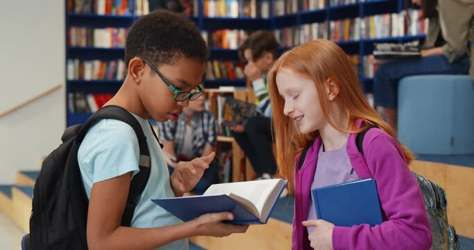 Multiethnic schoolchildren reading book and talking in library