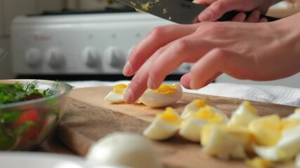 a cook in a bright kitchen cuts boiled eggs into wedges for salad. Female hands in a light kitchen cuts boiled eggs into wedges for salad. Close-up in slow motion, colorful - Powered by Adobe