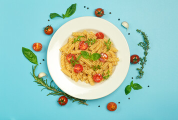 Food pasta on a blue background. Italian fusilli pasta with tomatoes, herbs and basil on a white plate. Healthy food concept.