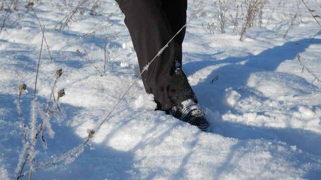 Male legs going uphill on snowy meadow. Fresh powder snow is blowing against sun reflection.