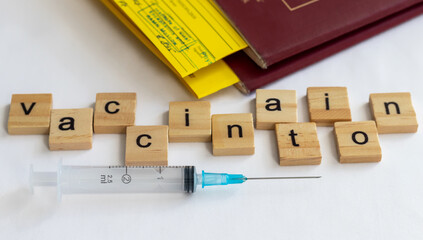 A syringe and wooden cubes with a set of letters of the word vaccination on the background of a tourist's passport with a yellow certificate. The concept of travel restrictions without vaccination.