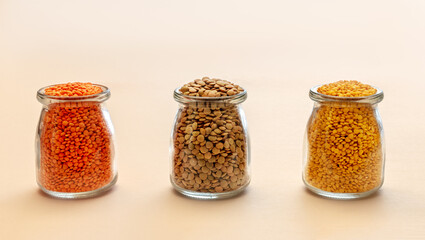Three glass jars with red, yellow and green lentils on a light background. Nutritious and Important Protein Source
