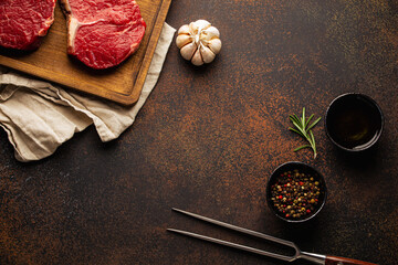 Cooking background for menu or template with raw meat steaks on wooden cutting board, spices and olive oil on rustic stone background with space for text 