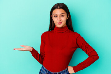 Young Indian woman isolated on blue background doubting and shrugging shoulders in questioning...