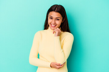 Young Indian woman isolated on blue background smiling happy and confident, touching chin with hand.