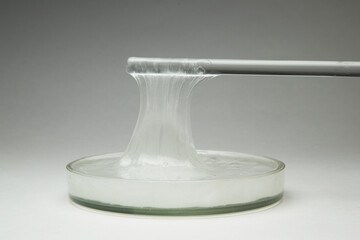 A close-up shot of a viscous white transparent chemical liquid like glue. The liquid is pulled with...