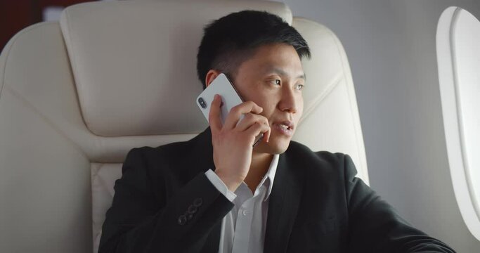 Asian businessman talking by phone on board of modern private airplane