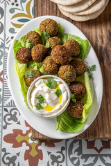 Traditional homemade chickpea falafel balls with white sauce and pita bread on whitw plate on wooden board, healthy vegetarian life concept. Israel Jewish food.