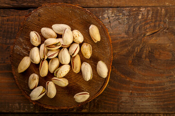 Fototapeta premium Pistachio nuts scattered on a round board on a wooden table.