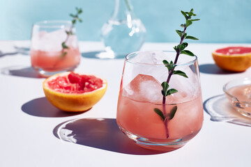 Summer grapefruit cocktail. Fresh healthy grapefruit beverage with herbs on sunlight with hard shadows. Creative drink on blue pastel background.