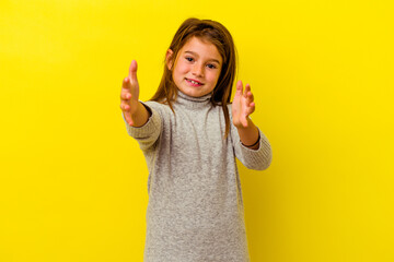 Little caucasian girl isolated on yellow background feels confident giving a hug to the camera.