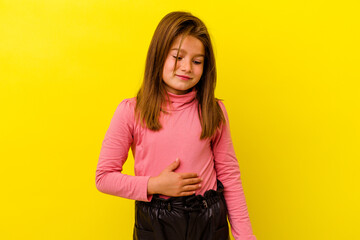 Little caucasian girl isolated on yellow background touches tummy, smiles gently, eating and satisfaction concept.