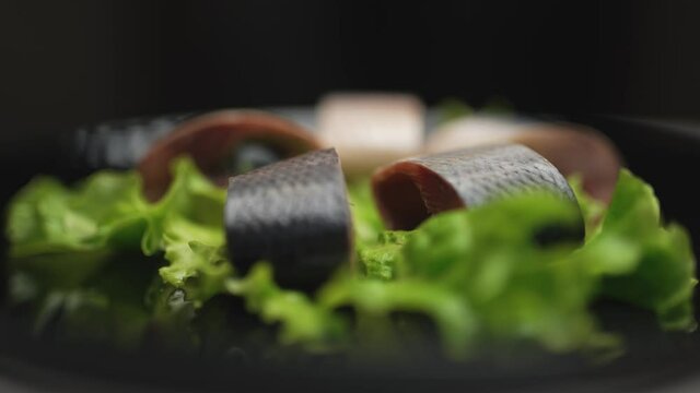 Close up herring in chunks with greens are rotating on the plate on black background. Healthy food clean eating selection.