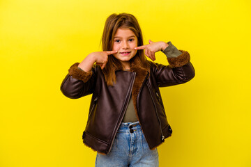 Little caucasian girl isolated on yellow background smiles, pointing fingers at mouth.